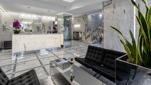 Una hall moderna con una reception in marmo, divani neri e un'ampia pianta in vaso.