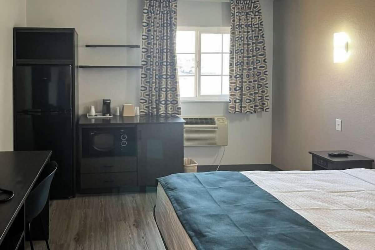 Una habitación compacta con cama, escritorio, kitchenette pequeño y ventana con cortinas estampadas.