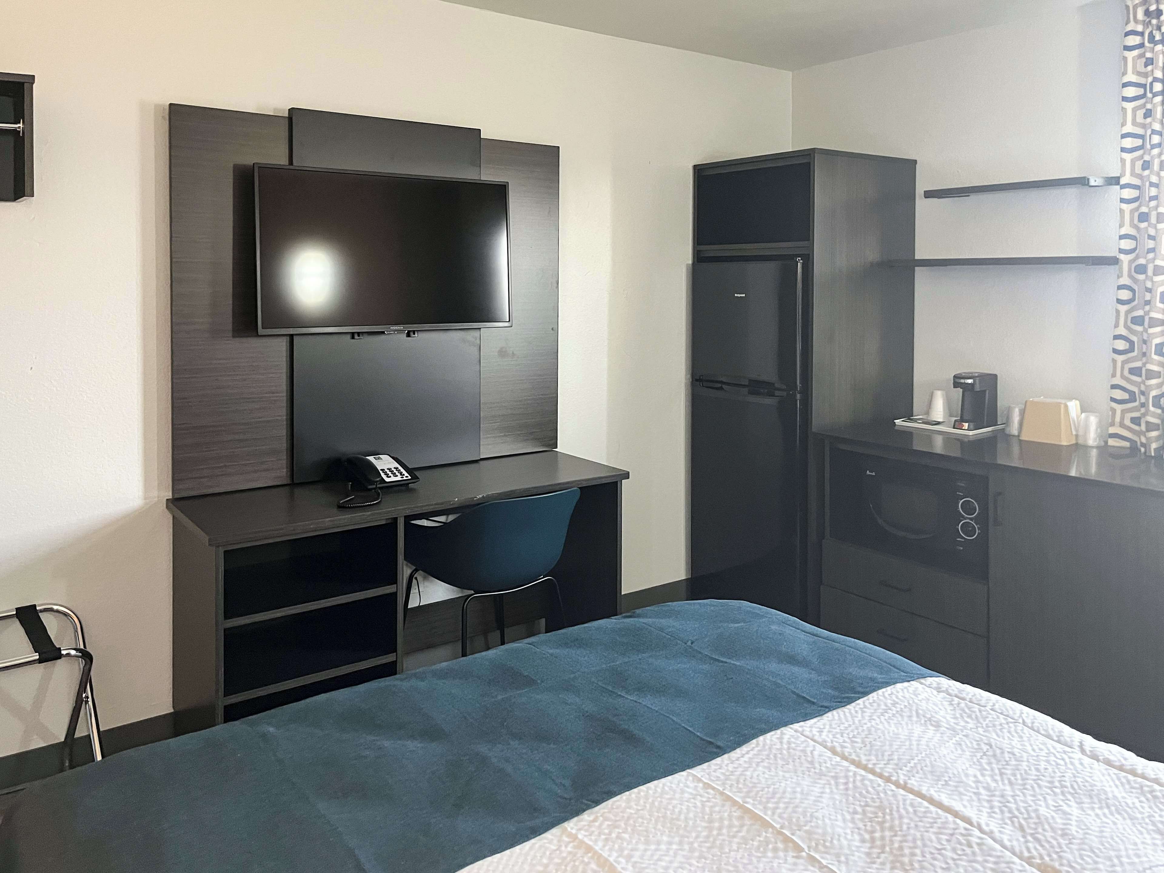 Ein Hotelzimmer mit einem Bett, einem Schreibtisch mit Stuhl, einem Fernseher, einem Kühlschrank und einer Kaffeemaschine.