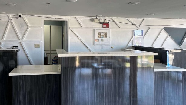 A reception desk with a modern design, a door leading to a room, and a fire alarm on the wall. - Studio 6 Suites Delano, CA (Delano)