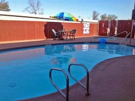Una piscina con valla, una mesa con sillas y un paraguas colorido.