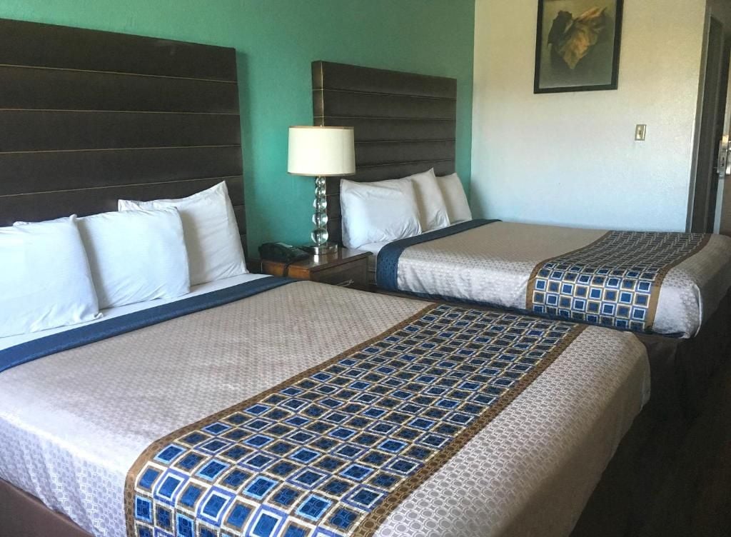 A hotel room with two beds, a nightstand, a lamp, and a painting on the wall.