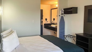 A hotel room with a bed, a desk, a mirror, and a bathroom visible through an open door. - Studio 6 Suites Delano, CA (Delano)