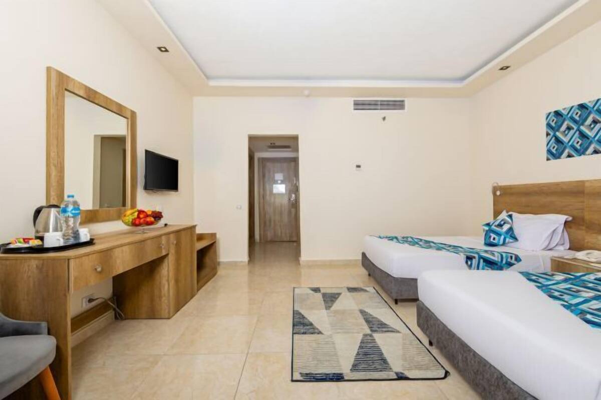 A hotel room with a wooden desk, two beds, a TV, and a fruit bowl.