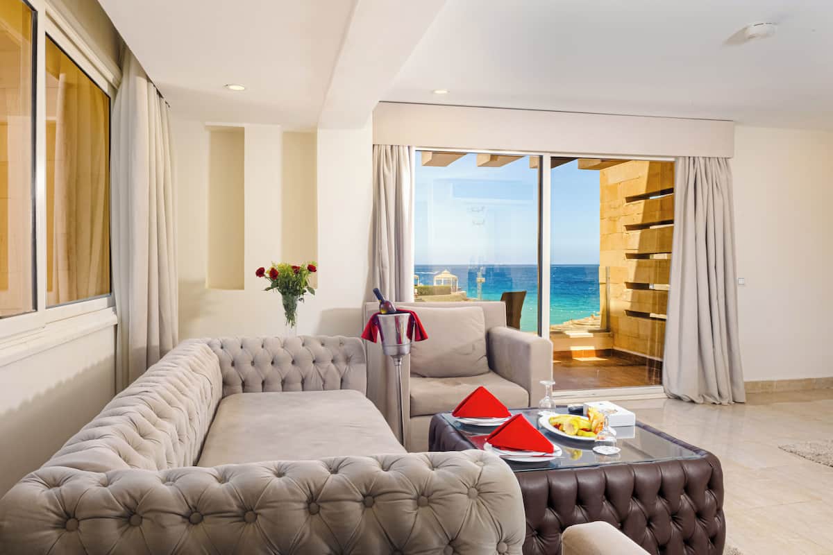 A modern living room with a large sofa, a coffee table, and a view of the ocean through large glass doors.