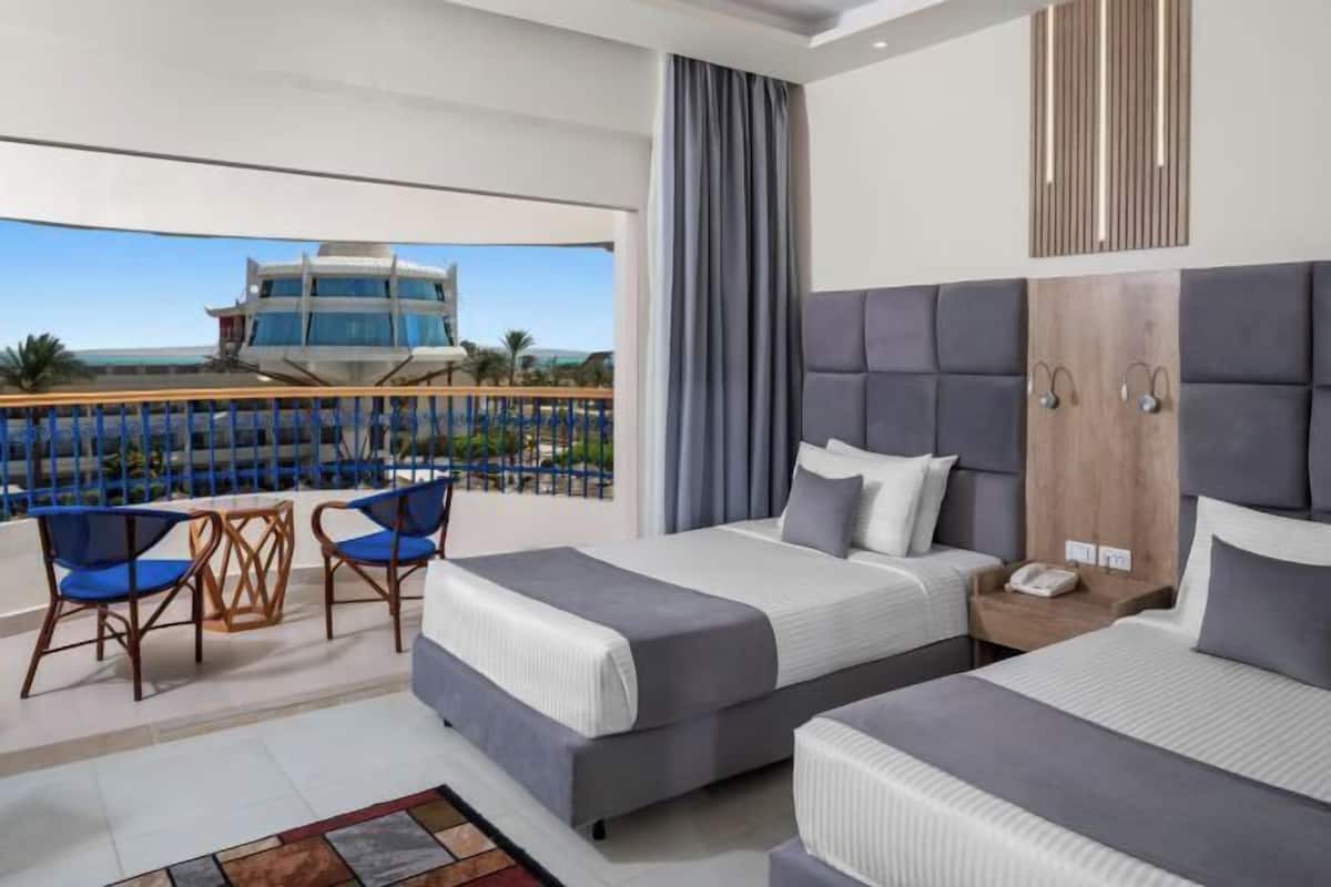 A hotel room with two beds, a balcony with chairs, and a view of a building.