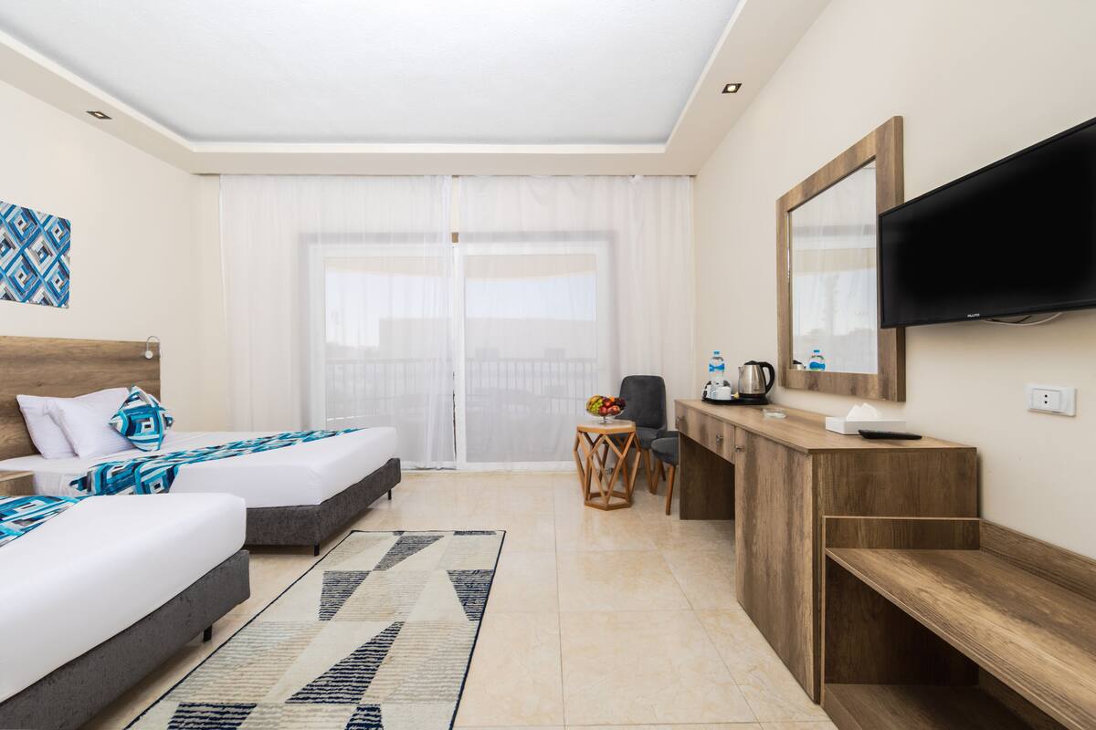 A hotel room with two beds, a desk, a TV, and a large window.