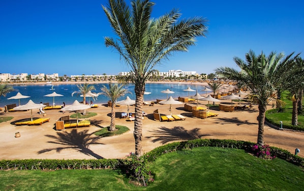 Un complejo turístico en la playa con tumbonas, sombrillas y palmeras.
