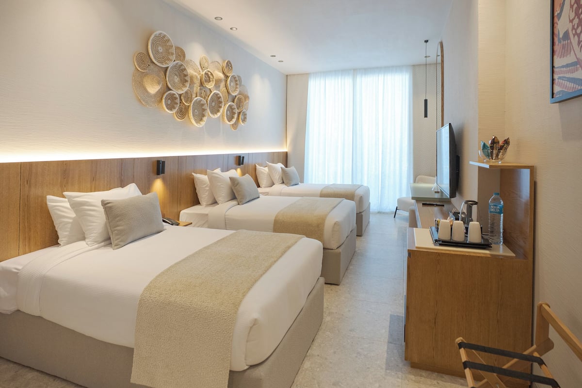 A hotel room with two beds, a desk, a TV, and a wall art piece.