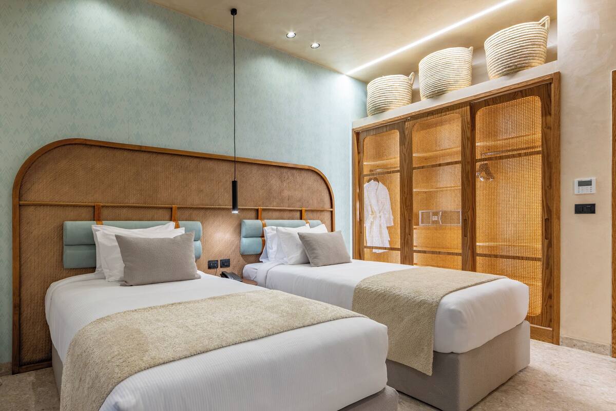 A hotel room with two beds, a wooden headboard, a wardrobe, and a ceiling light.