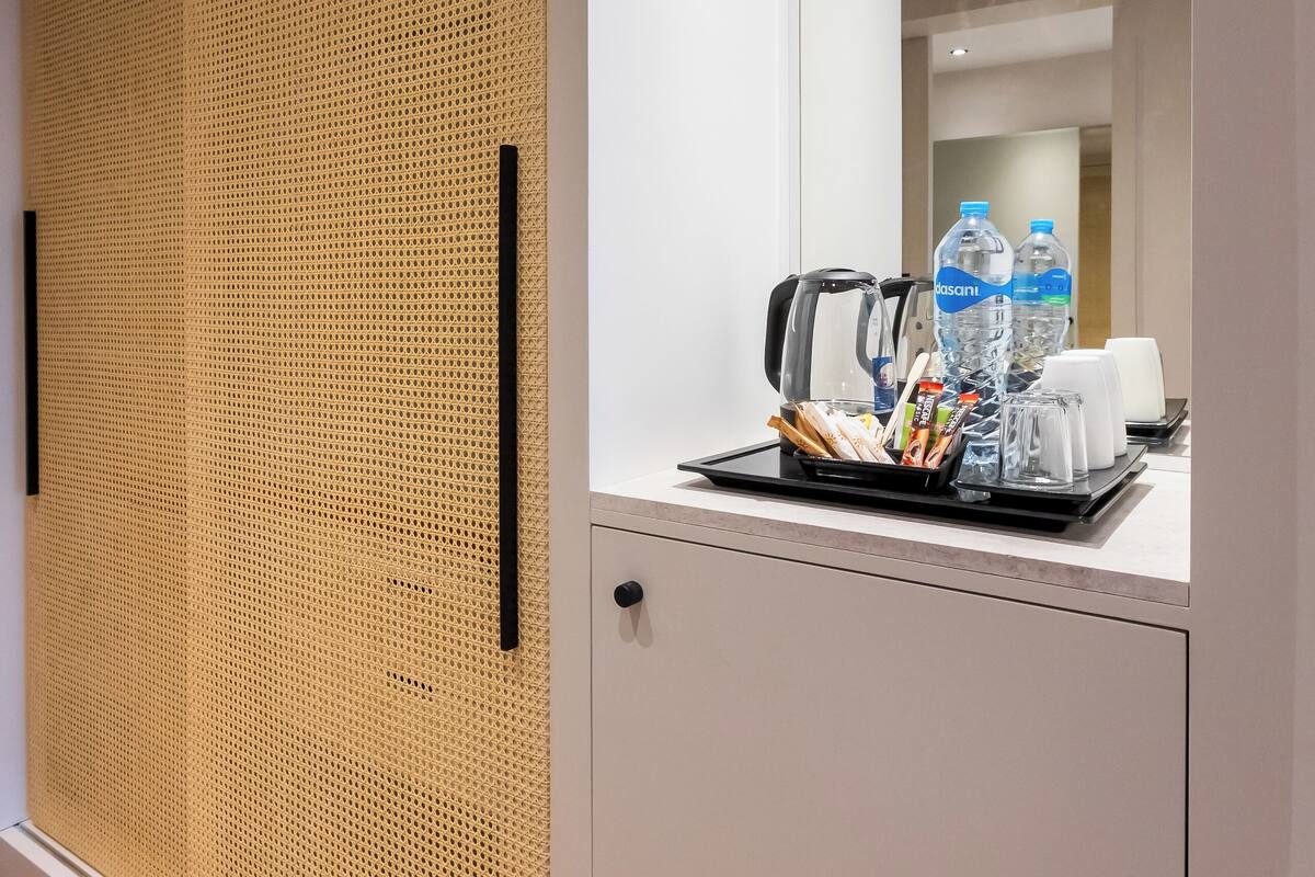 A modern hotel room with a large mirror, a wooden partition, and a tray with toiletries and a kettle.