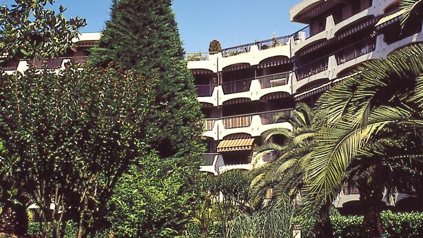 A multi-story hotel with balconies, surrounded by lush greenery and palm trees. - Résidence Lagrange Vacances Les Trois Rivières (Mandelieu-La-Napoule)