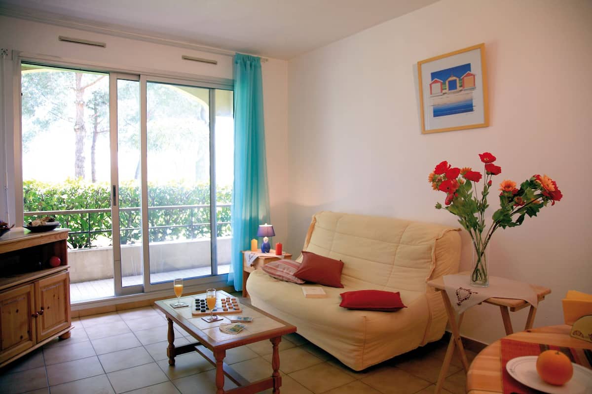 A living room with a sofa, a coffee table, a small table with drinks, a vase with flowers, and a painting on the wall.