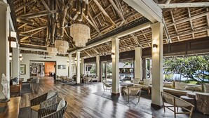 Un hall espacioso con suelo de madera, muebles de mimbre y un techo alto con vigas a la vista y candelabros.