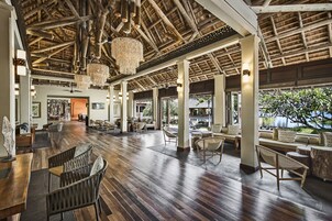 Un hall espacioso con suelo de madera, muebles de mimbre y un techo alto con vigas a la vista y candelabros.