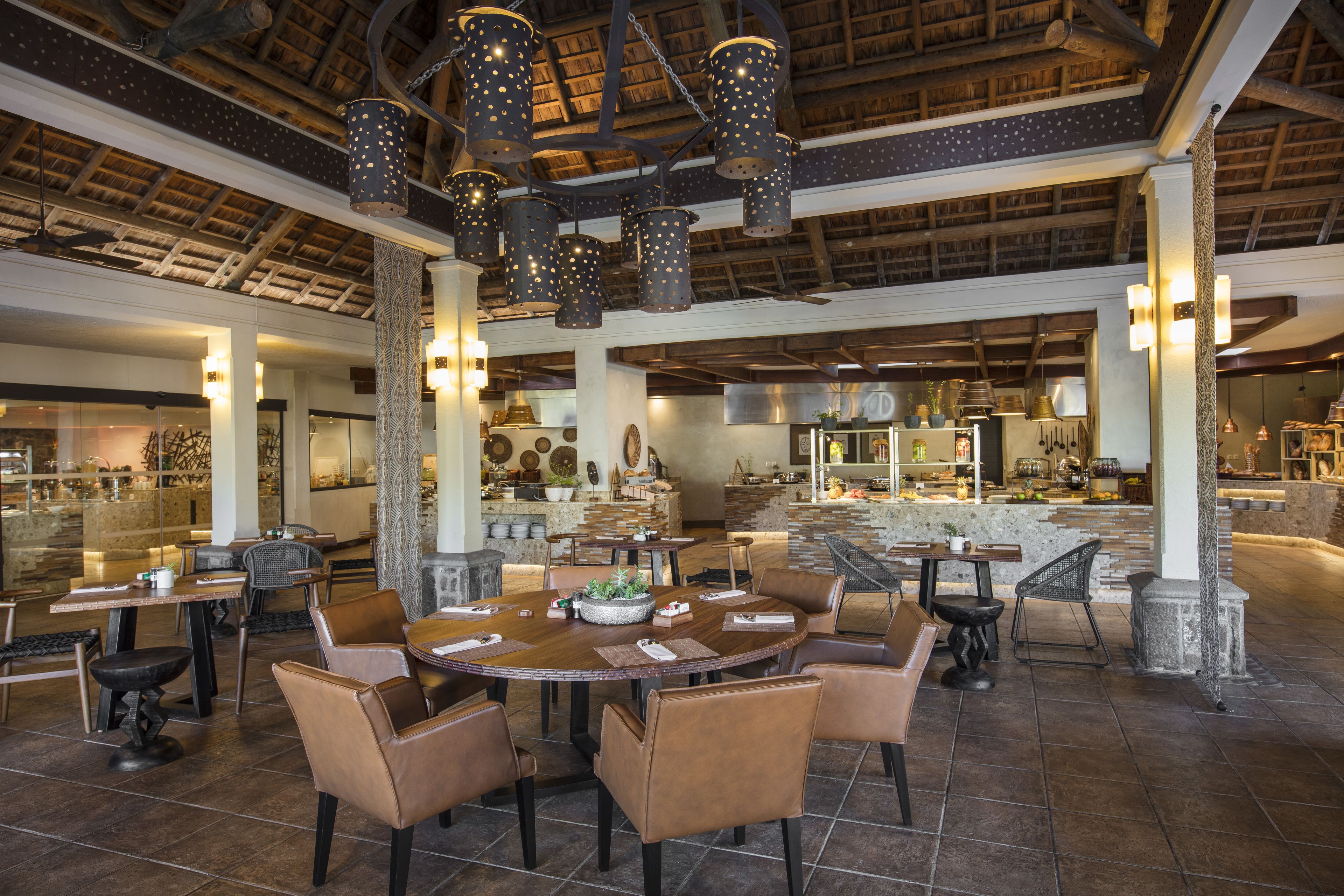 A spacious dining area with high ceilings, exposed beams, and a central round table surrounded by leather chairs.