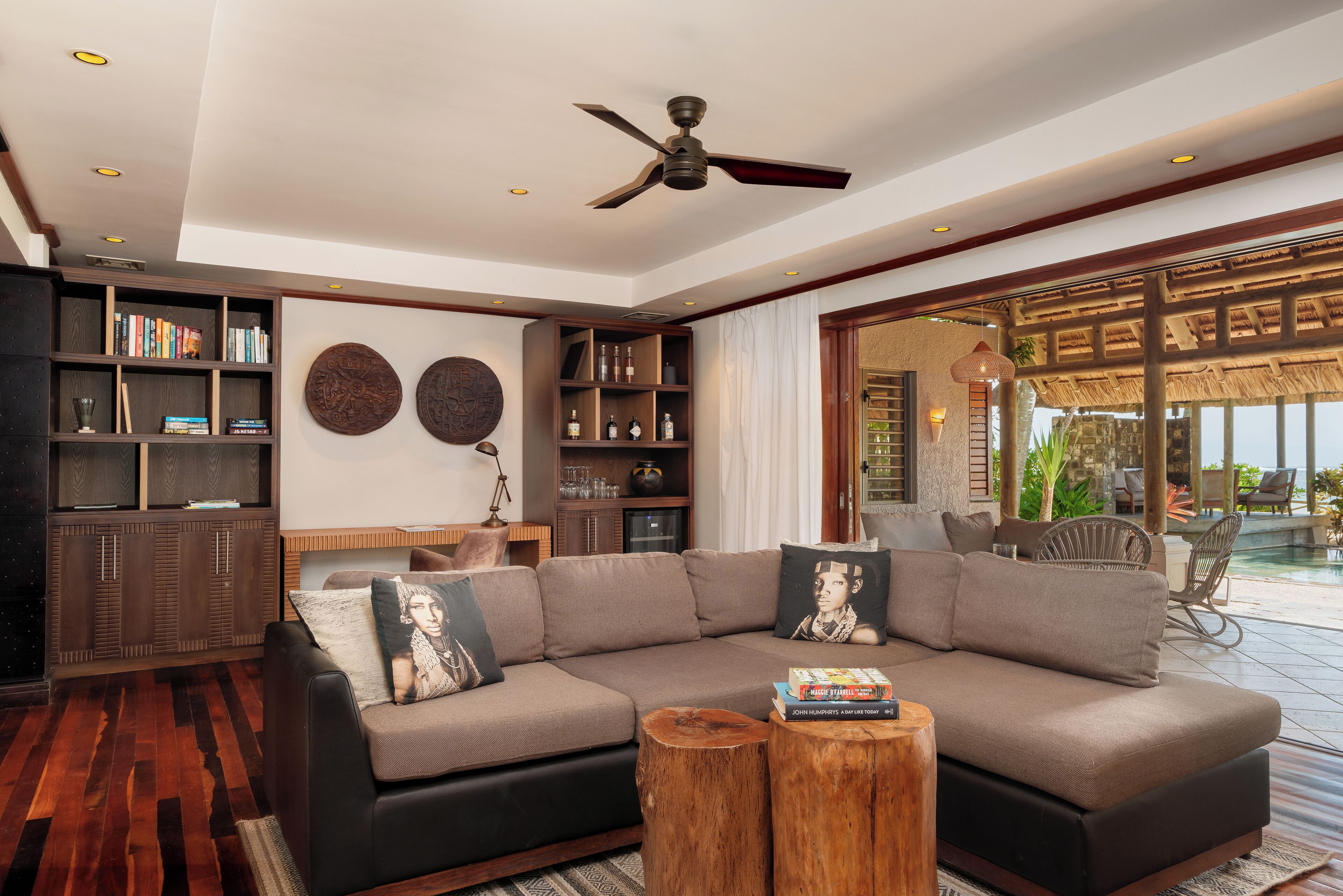 A modern living room with a sectional sofa, wooden bookshelves, and a ceiling fan.