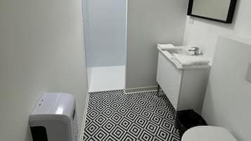 A modern bathroom with a geometric patterned floor, a white toilet, a sink with a mirror, and a hand dryer.