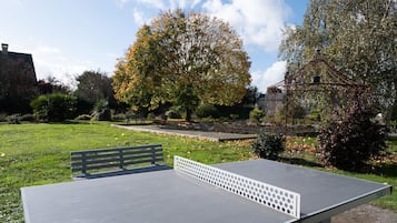 A ping pong table in a park with a bench and trees in the background.