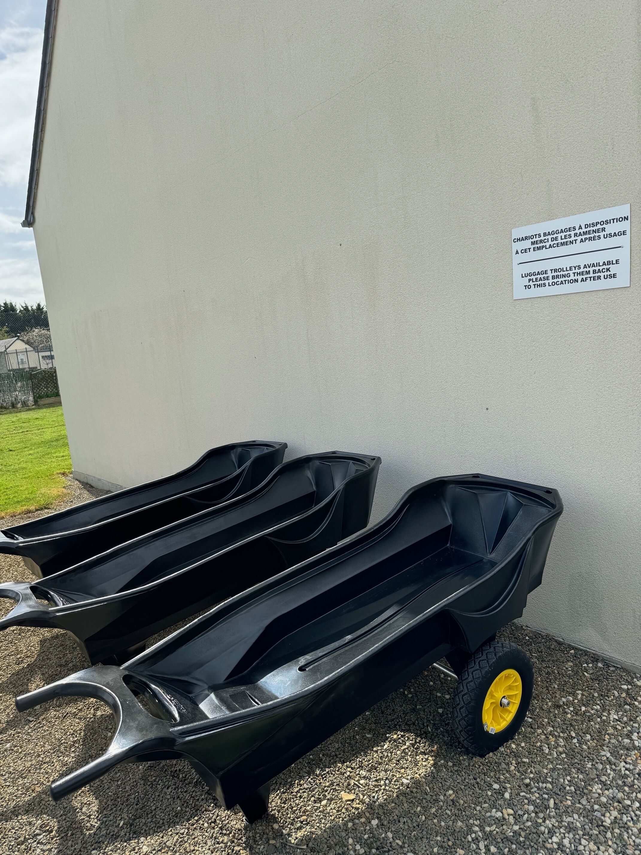 Een zwarte bagagetrolley met een geel wiel geparkeerd tegen een muur met een bord in het Frans.