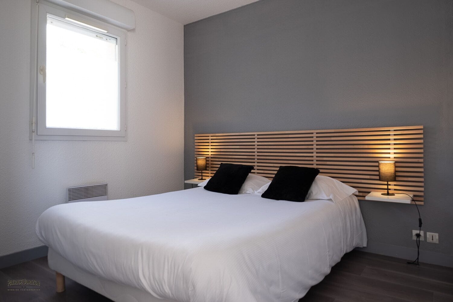 A neatly made bed with white linens, a headboard with horizontal slats, and two bedside lamps.