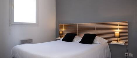 A neatly made bed with white linens, a headboard with horizontal slats, and two bedside lamps.