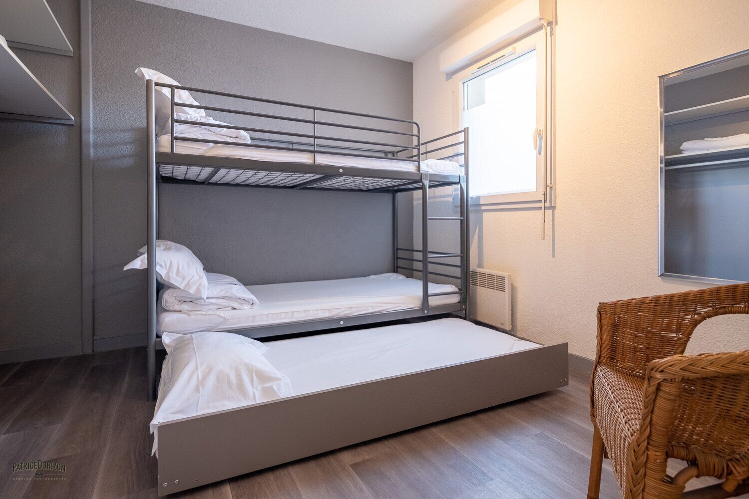 Una camera con un letto a castello, una sedia in vimini e una finestra.
