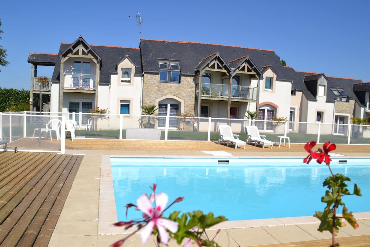 Un espace piscine doté d’une terrasse en bois et de chaises longues, le tout entouré d’une clôture blanche.