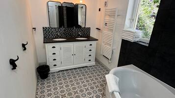 A bathroom with a black and white patterned floor, a white vanity with a mirror, and a bathtub.
