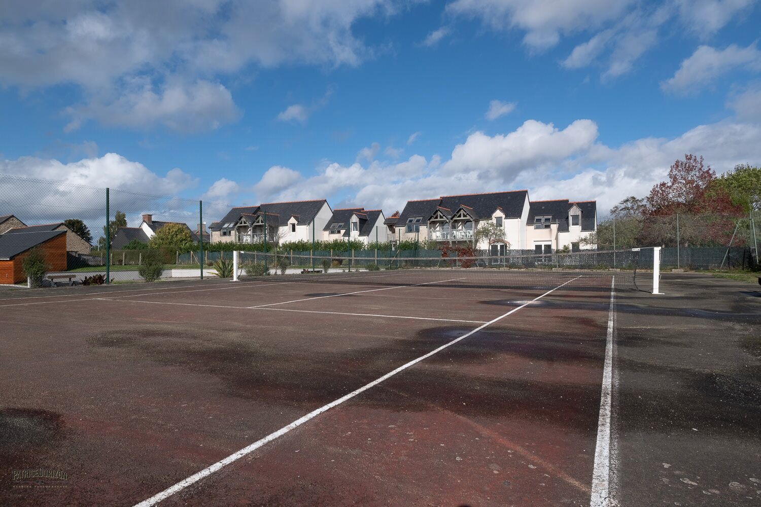 Ein Tennisplatz mit Netz, umgeben von Häusern mit geneigten Dächern.