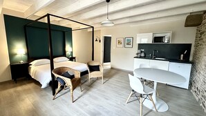 A modern bedroom with a four-poster bed, a small dining table, and a kitchenette. - Appart'Hôtel Mont Saint Michel Résidence Fleurdumont (Beauvoir)