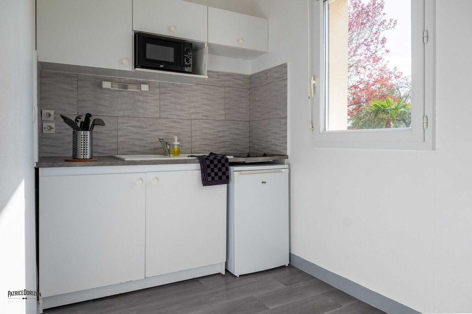 Una cocina compacta con armarios blancos, un microondas y un refrigerador pequeño.