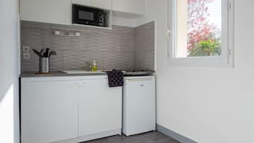 Una cocina compacta con armarios blancos, un microondas y un refrigerador pequeño.