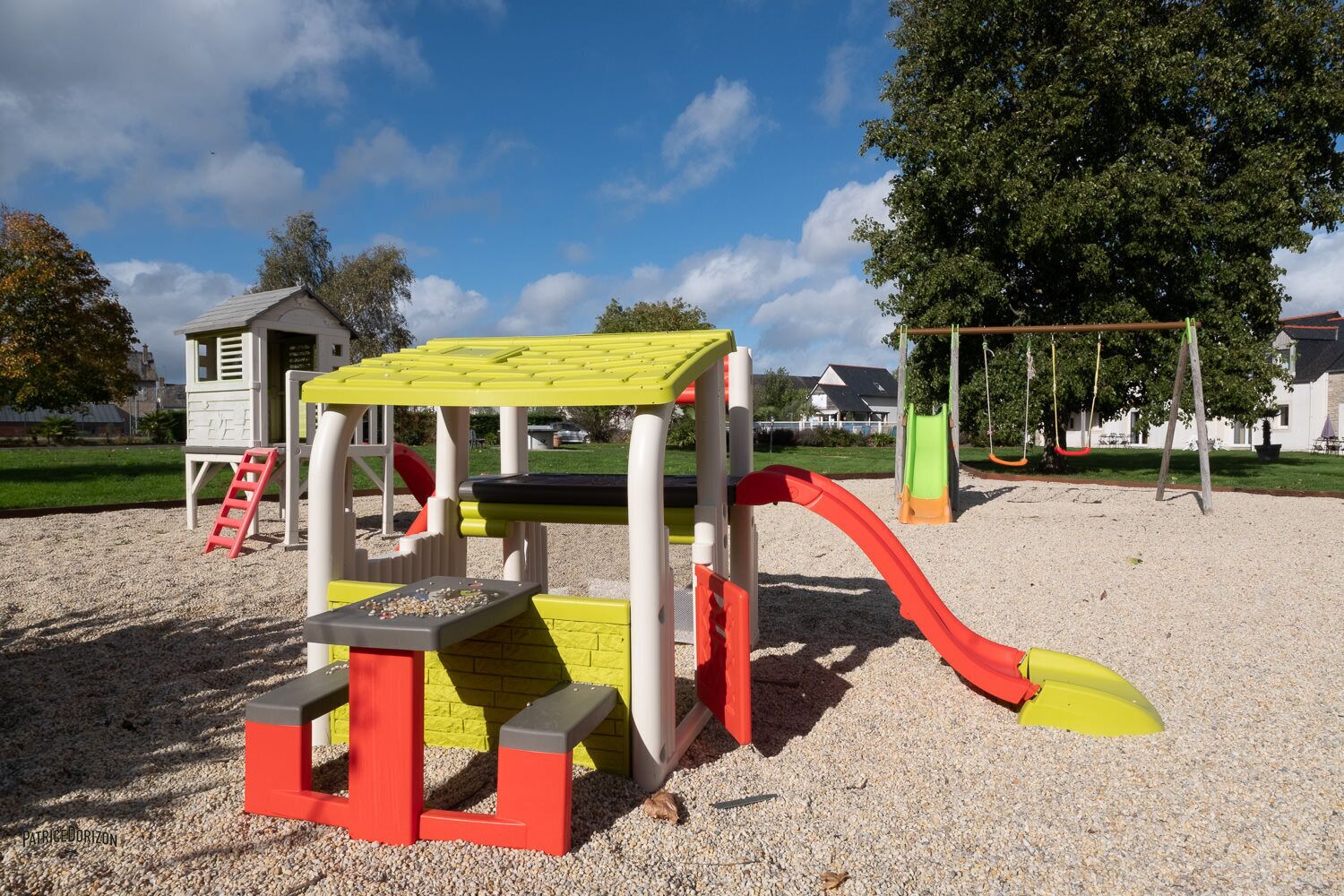 A playground with a climbing structure, slides, and a small building.