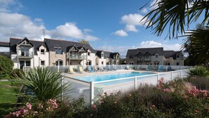 A pool area with lounge chairs, a clear sky, and a row of houses in the background. - Appart'Hôtel Mont Saint Michel Résidence Fleurdumont (Beauvoir)