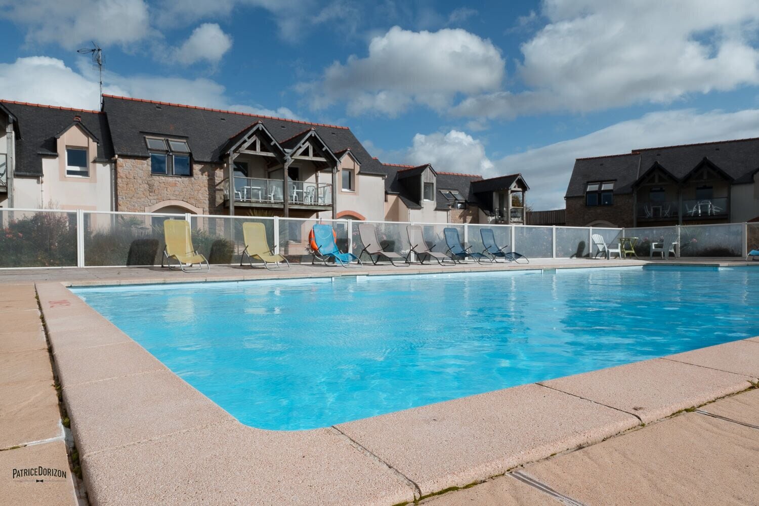 A swimming pool with lounge chairs and a building with balconies in the background.