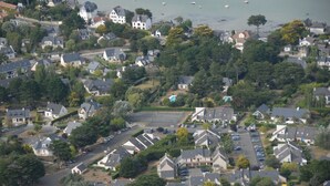An aerial view of a residential area with houses, a central green space, and a body of water with boats.