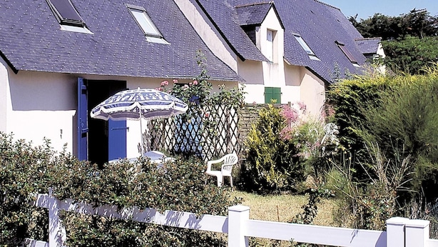 A house with a sloped roof, a white fence, and a garden with various plants and a bench.
