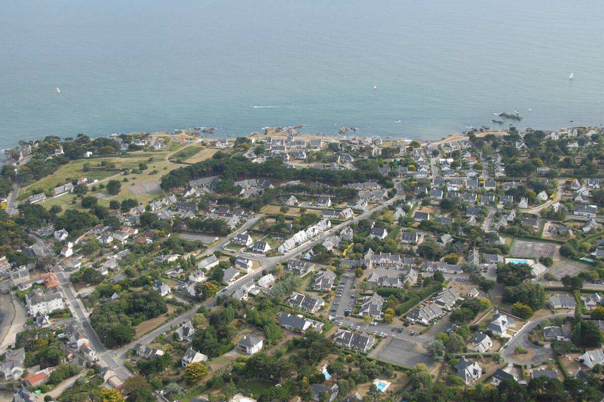 An aerial view of a coastal residential area with houses, roads, and a beach.
