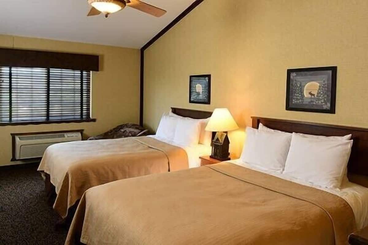 A hotel room with two beds, a ceiling fan, a window with blinds, and a wall-mounted picture.