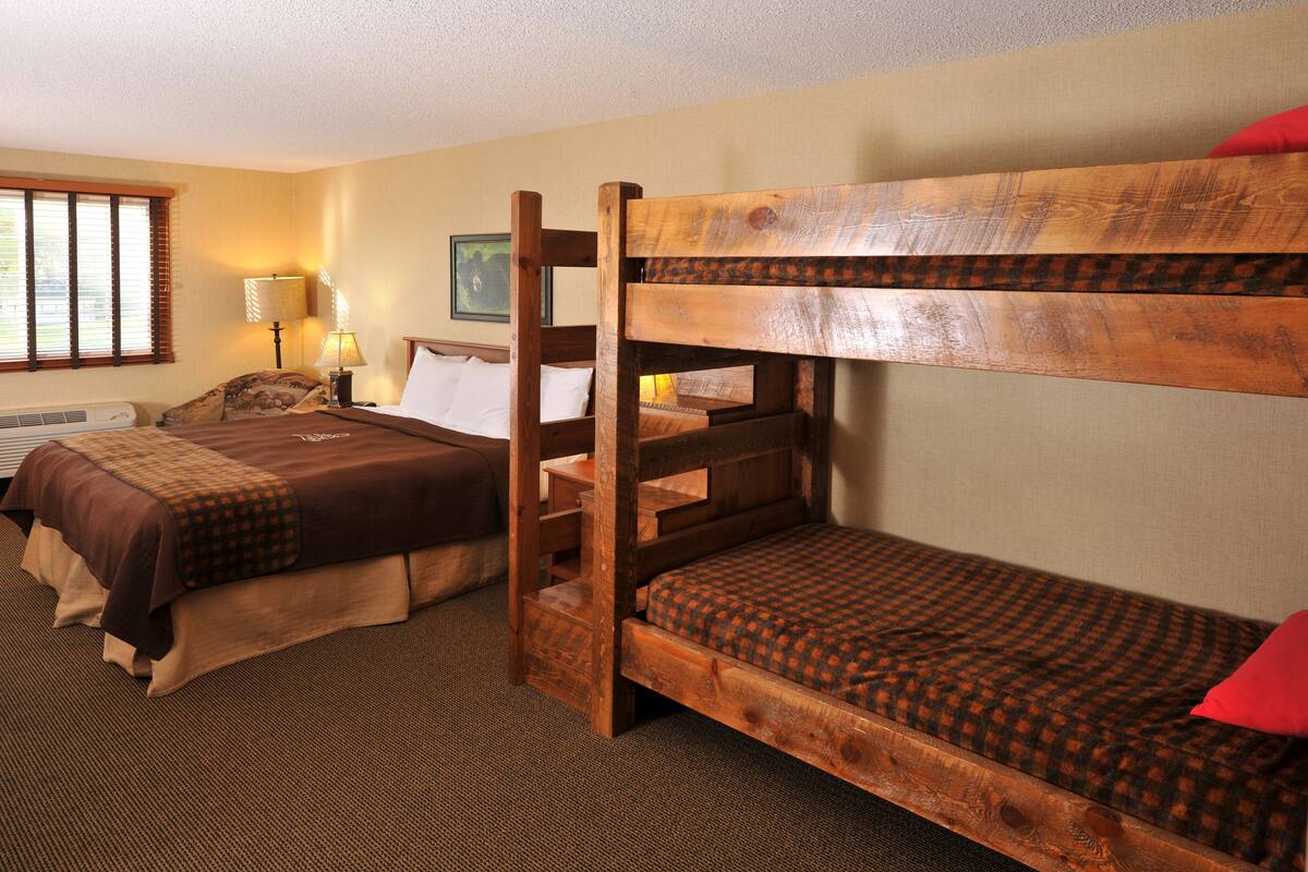 A room with two bunk beds, a bedside table with a lamp, and a window with blinds.