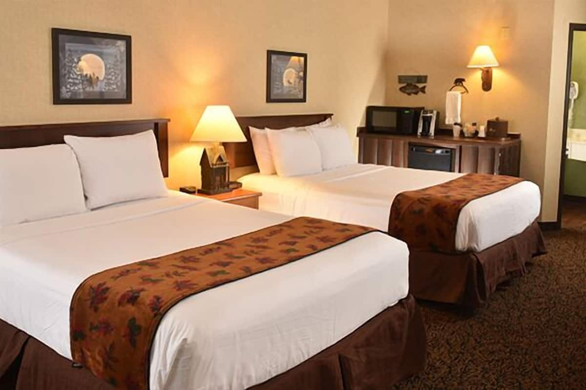 A hotel room with two beds, a desk, a lamp, a television, and artwork on the walls.