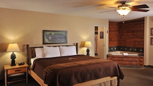 A hotel room with a large bed, two bedside tables with lamps, a painting on the wall, and a wooden wall paneling. - Boarders Inn & Suites by Cobblestone Hotels – Waukon (Waukon)