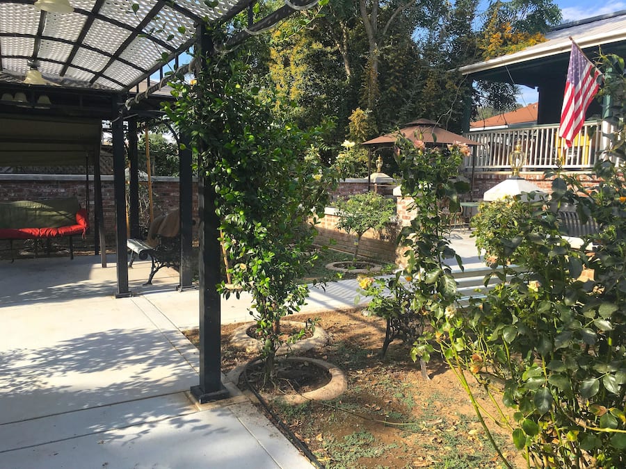 A covered patio area with a bench, a small tree, and a flag.