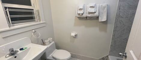A bathroom with a toilet, sink, and shower. There are towels hanging on the wall.