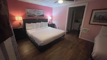 Un dormitorio con cama, mesitas de noche, ventilador de techo y puerta que da al baño.