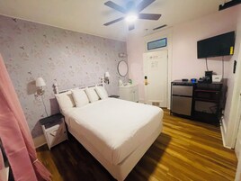Un dormitorio con una cama, un escritorio, un ventilador de techo, un televisor y una puerta.