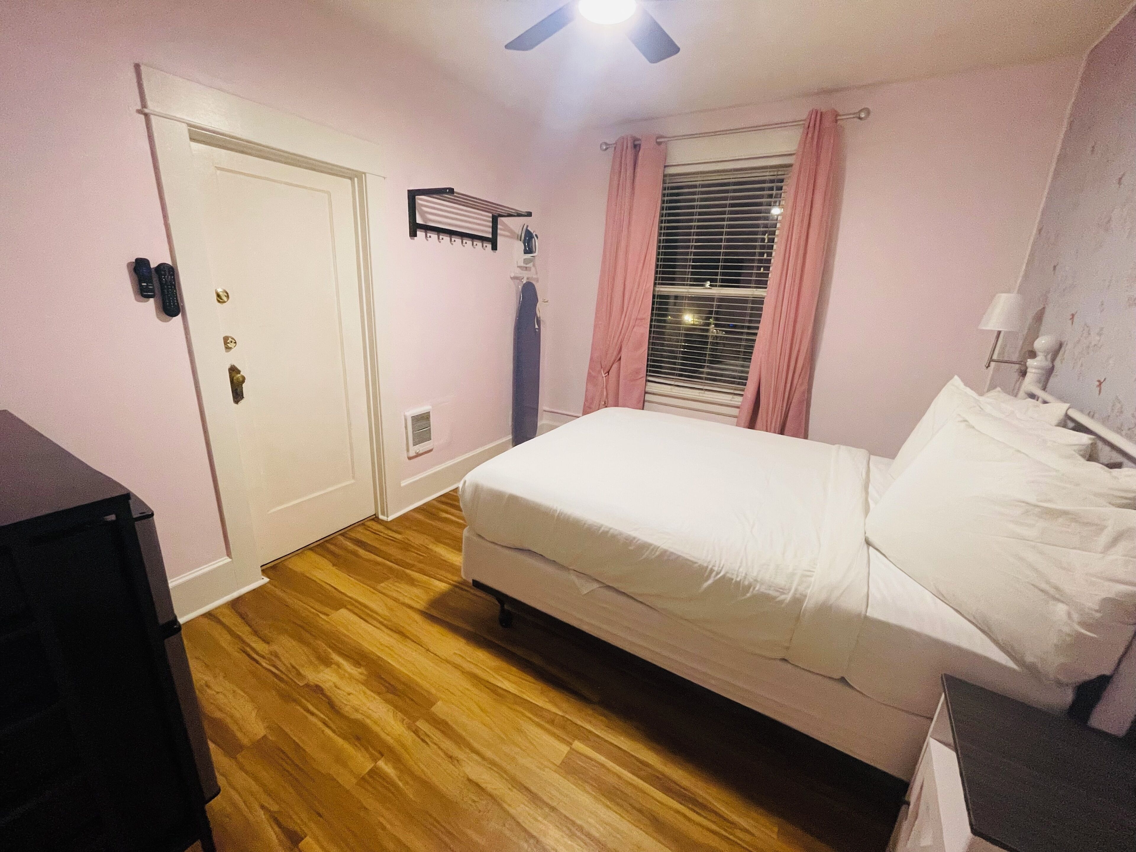 Una camera da letto con un letto, una porta, una finestra con tende e un comodino.