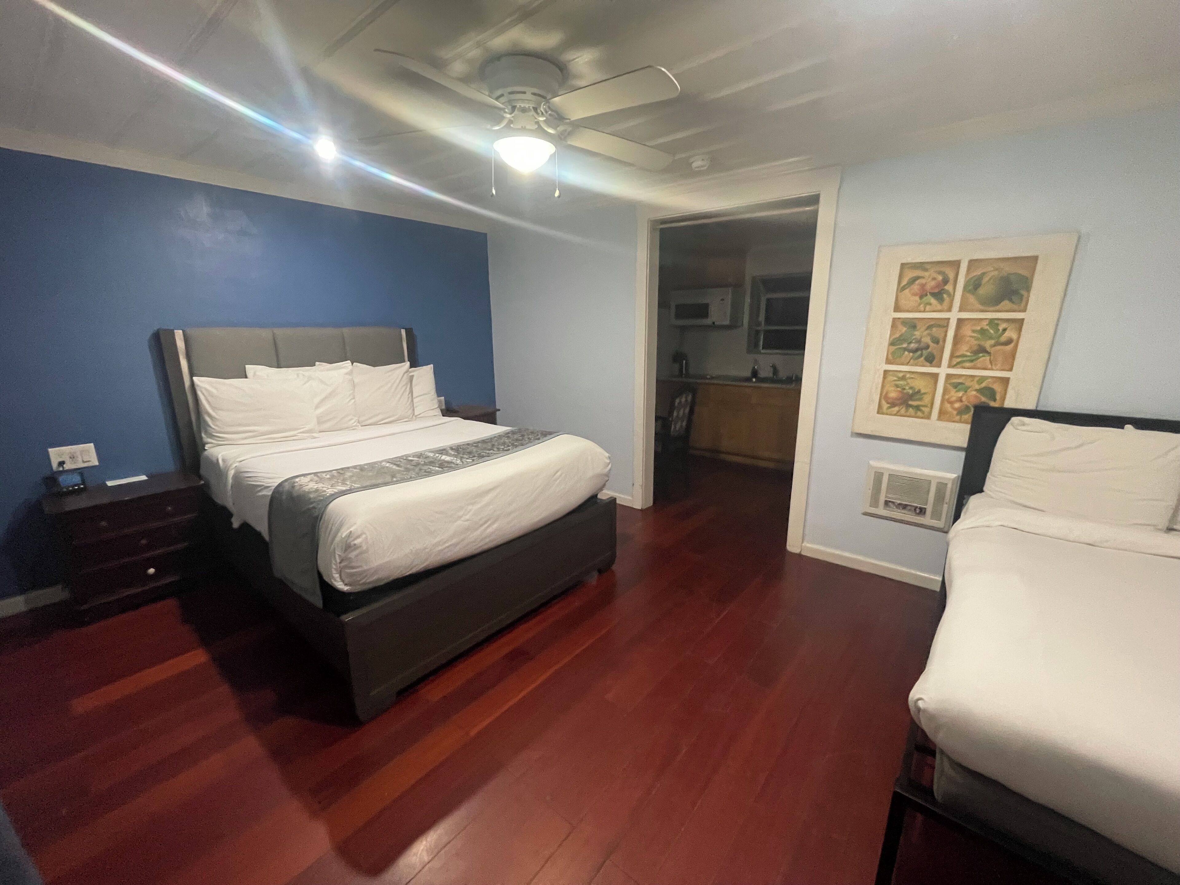 Ein Hotelzimmer mit einem großen Bett, einem Nachttisch, einem Deckenventilator und Blick zur Küche.