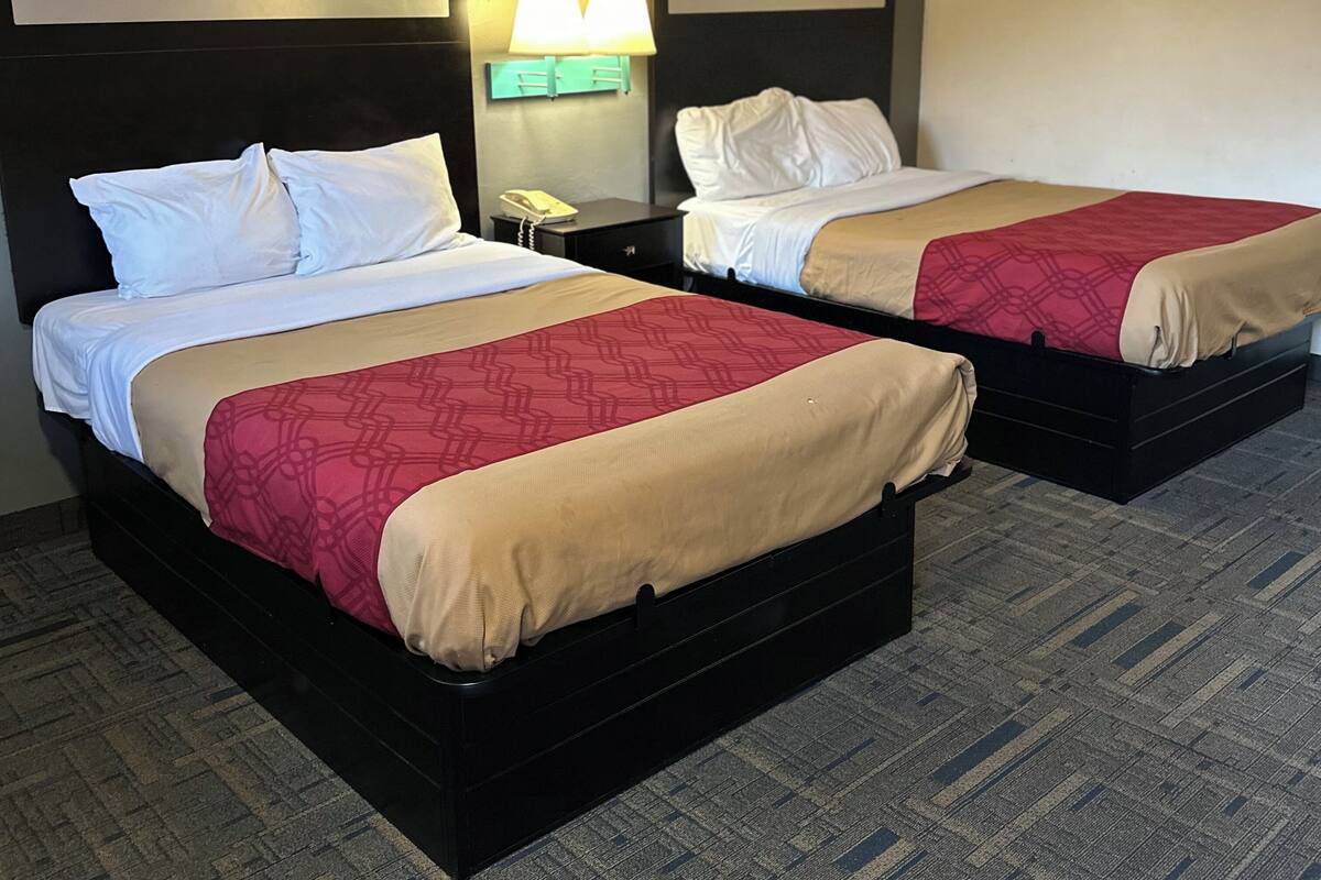 A hotel room with two beds, each with a headboard, a nightstand with a lamp, and a telephone.